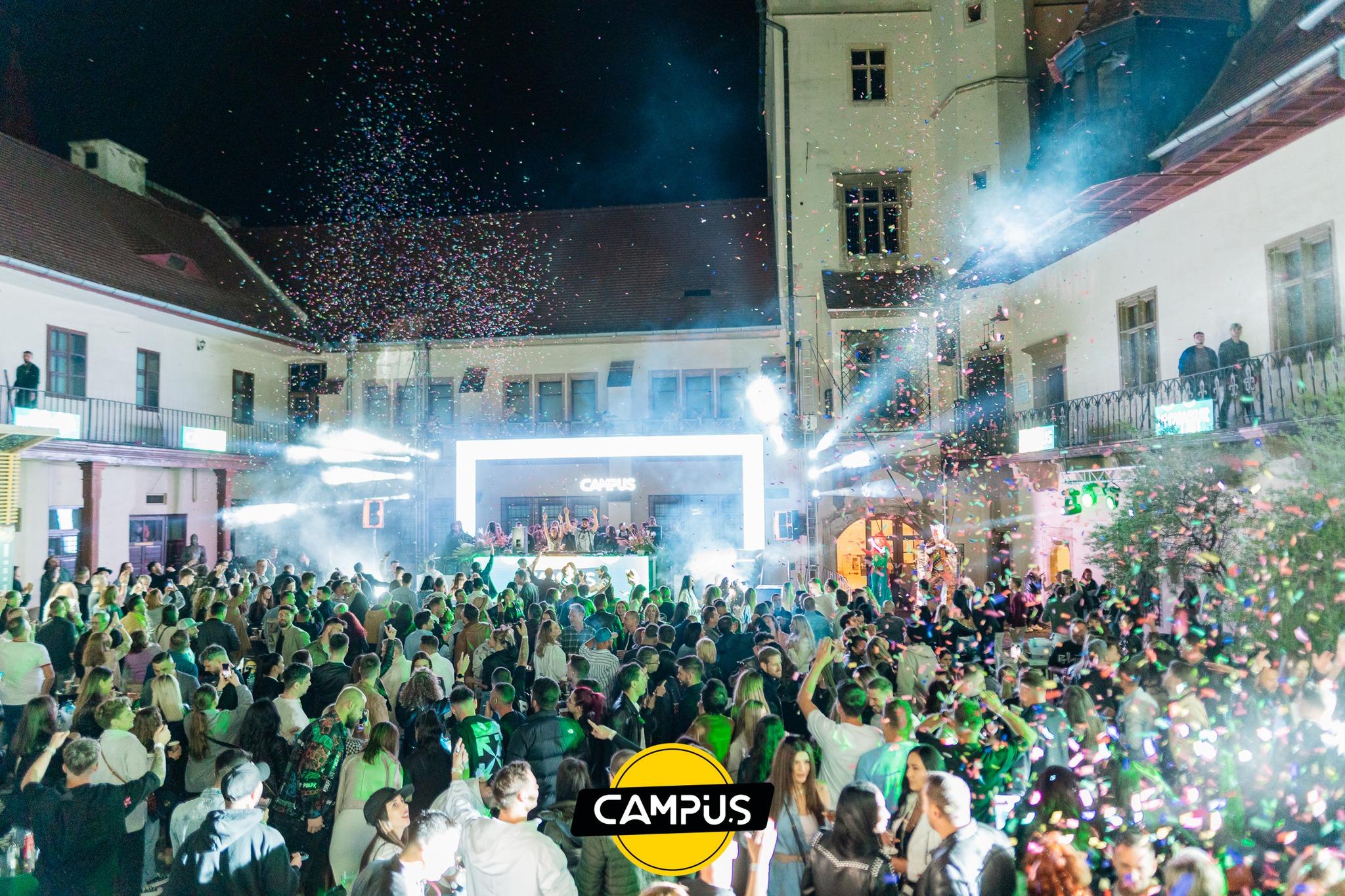 Curte istorică plină de oameni, cu scenă luminată, fum și confetti în aer
