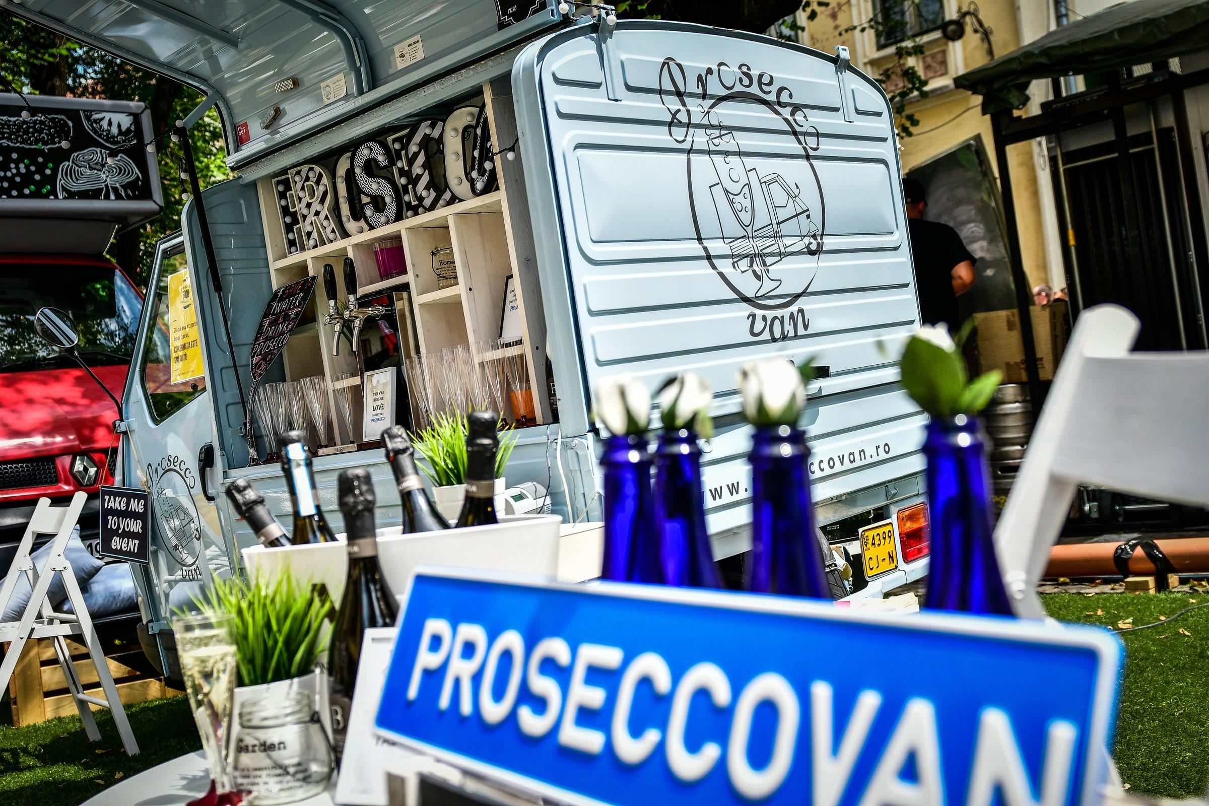 Rulotă-bar de prosecco, cu sticle la gheață și pahare pregătite, într-o grădină